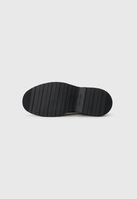 Black rubber shoe sole with horizontal grooves, featuring a slight arch and a rounded toe. "Calvin Klein" logo embossed near the heel.