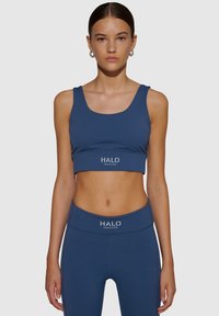 Marinblå sportbh i stretchy tyg med rundad halsringning och logodetalj längst ner, ihop med matchande högmidjade leggings.