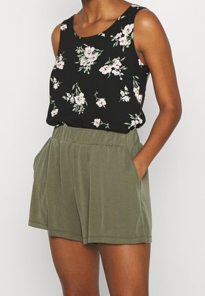 Mouwloze zwarte top met witte en roze bloemenprint, gecombineerd met losse, olijfgroene shorts met hoge taille en zijzakken.