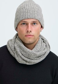 Beanie a coste grigia e sciarpa infinita abbinata. Texture morbida, design ad anello e filato misto. Indossato sopra un maglione nero.