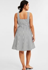 Zwart-witte geblokte jurk met een vierkante rug, getailleerde bodice, uitlopende rok en brede schouderbanden. Het materiaal lijkt lichtgewicht en glad te zijn.