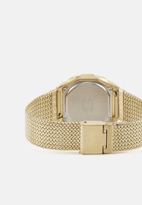 Guldtonad klocka med meshband, oktagonal klockkapsel och en polerad baksida. Har ett spänne med märket "CASIO" ingraverat.