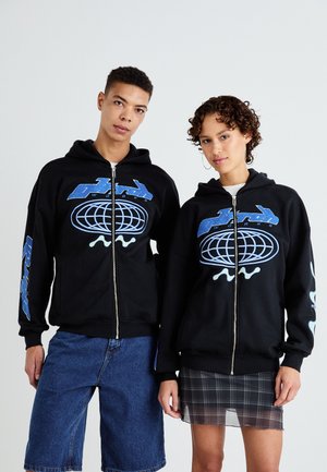Black zip-up hoodies feature blue graphic designs, including a globe and lettering, with ribbed cuffs. Pair worn with denim shorts and a plaid skirt.