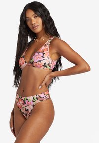 Kvetinový bikiny set s ružovým pozadím a veľkými mnohobarevnými kvetmi. Vrchná časť má hlboký V-výstrih a široké ramienka, zatiaľ čo spodná časť je nízko vyrezaná.