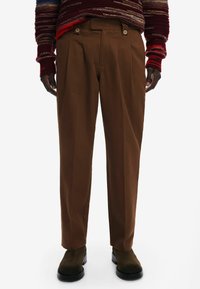 Brązowe spodnie w kant wykonane z fakturowanej tkaniny, z guzikami na pasku, zestawione z czarnymi botkami za kostkę.