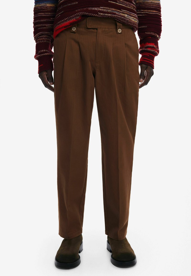 Brązowe spodnie w kant wykonane z fakturowanej tkaniny, z guzikami na pasku, zestawione z czarnymi botkami za kostkę.