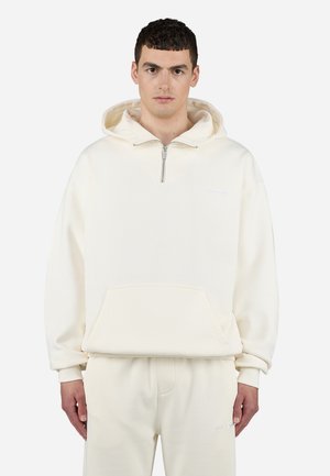 Light beige hoodie with a half-zip design, front pocket, and ribbed cuffs. Soft fabric with a minimal logo on the chest. Paired with matching pants.