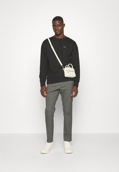 Zwarte sweatshirt, grijze op maat gemaakte broeken en witte sneakers. Kleine lichtgekleurde schoudertas met handvatten. Eenvoudig ontwerp en effen kleuren.