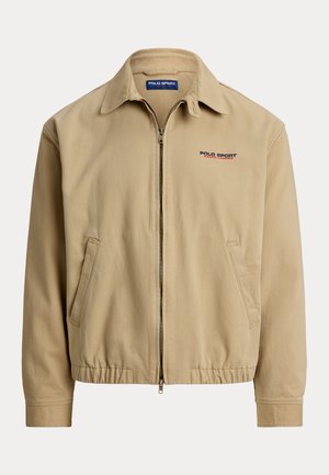 Beige jakke med krave, lynlås foran og elastiske manchetter. Har sidelommer og "Polo Sport"-logo i rød og blå.