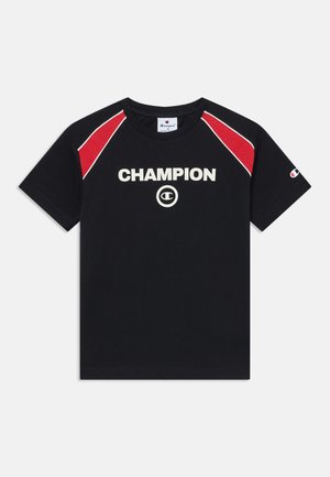 Črna bombažna majica s kortami rdeče mreže na ramenih. Na sprednji strani se nahaja beli logo "CHAMPION" in majhen logo na rokavu.