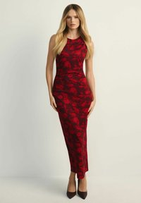 Czerwona sukienka w kwiaty o dopasowanym kroju, bez rękawów, maxi długości. Gładka tekstura, zestawiona z ciemnymi butami na wysokim obcasie.