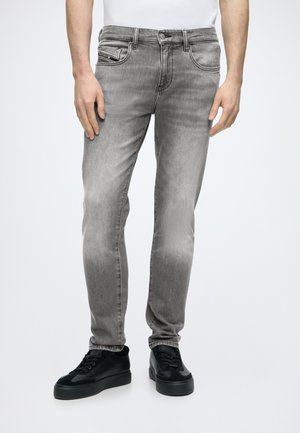 Homme portant un jean gris délavé slim et des baskets noires sur fond blanc uni.