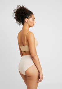 Reggiseno color nude e slip a vita alta, design senza cuciture, texture morbida, stile aderente, spalline regolabili, dettagli di cucitura minimi.