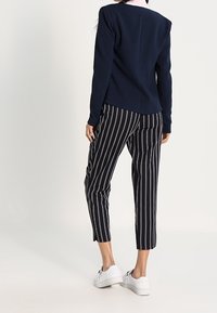 Blazer bleu marine à la coupe ajustée, porté avec un pantalon fuselé rayé noir et blanc et des baskets blanches. Tissu lisse avec des détails sur mesure.