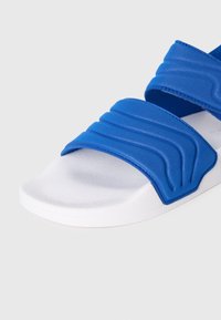 Γαλάζια σανδάλια με λουράκια με υφή, σχεδιασμένα με κυματιστό μοτίβο. Η σόλα είναι λευκή, με λεπτή, αντιολισθητική υφή για καλύτερη πρόσφυση.