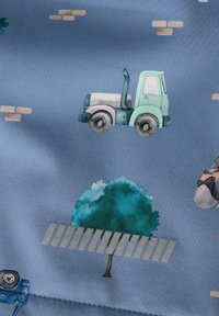 Camion jouet vert et blanc sur un fond bleu avec un arbre, une clôture grise et des briques marron clair éparpillées.