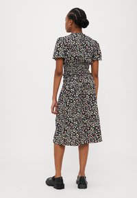 Svart blomstermønsteret kjole med korte ermer, smocket midje og midi lengde. Små flerfargede blomster over stoffet. Kombinert med svarte sko.