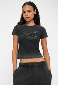 Zwart cropped t-shirt van zachte stof, met de tekst "Forever Hugo" in metalen draad. Korte mouwen en geribbelde halslijn.