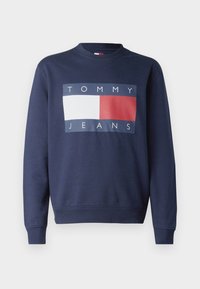 Felpa blu navy con collo a giro, caratterizzata da un grande logo rettangolare con il testo "TOMMY" e "JEANS" in bianco, blu e rosso.