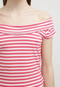 Pruhovaná off-the-shoulder blůza s růžovými a bílými horizontálními pruhy, měkkou texturou a krátkými rukávy s volánkovým akcentem.