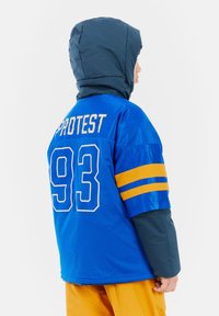 Blaue Sportjacke mit Netzstruktur, mit gelben Streifen an den Ärmeln, dem Text "PROTEST" und der Nummer "93" auf dem Rücken. Mit Kapuze.