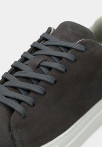 Mørkegrå semsket sneakers med matchende snørebånd og en hvit gummisåle, vist i nærbilde fra oversiden.