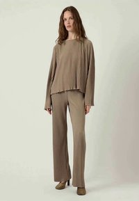Brown, pleated long-sleeve top and matching trousers. Soft fabric with a relaxed fit. Subtle texture and wide-leg design. Heeled shoes.
