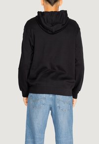 Felpa nera con cappuccio ampio, vestibilità comoda e polsini in costina, abbinata a jeans denim blu chiaro con tasche posteriori.