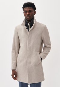 Abrigo de lana gris claro con un alto cuello, cierre de cremallera, bolsillos laterales y una silueta estructurada. Textura suave y diseño minimalista.
