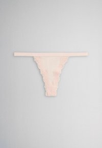 Light pink lace-trimmed thong underwear with a thin waistband laid flat on a plain grey background.
