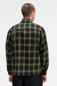 Camisa de flanela de xadrez em tons de preto e amarelo. Apresenta um corte relaxado, mangas longas e detalhes de punhos com botão. Tecido texturizado com um padrão de xadrez clássico.