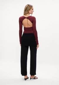 Bordo longsleeve z węzłem z tyłu, w połączeniu z czarną warstwową spódnicą i czarnymi sandałami na obcasie. Gładki materiał, dopasowana sylwetka.