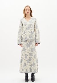 Maglione grigio con texture e gonna lunga abbinata, entrambi con un motivo floreale bianco in rilievo. La modella indossa stivali neri fino al ginocchio.