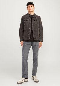 Black denim jacket with front pockets, gray t-shirt, gray jeans, and beige sneakers. Model stands on a plain background.