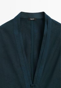 Tmavě tyrkysový kimono stylový kabát s texturovaným vzorem, zdobený klopovým límcem a předním zapínáním. Podšívka s jemným leskem.