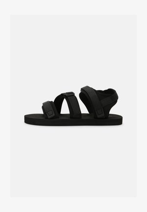Black sandals with three adjustable strap closures, flat sole, and a textured footbed for grip. Made of soft materials for comfort.