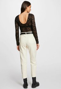 Top lungo a maniche in pizzo nero con scollatura a barca, abbinato a pantaloni bianchi aderenti e stivaletti neri alla caviglia, con una cintura in vita.