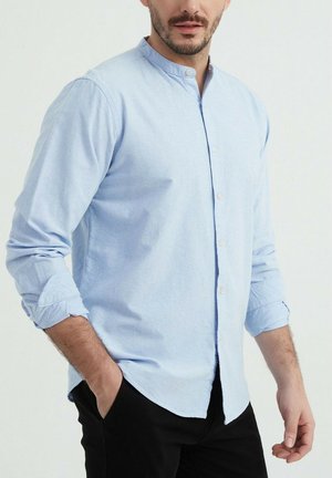 Chemise à manches longues bleu clair avec col montant, boutons sur le devant et manches retroussées, fabriquée en coton doux.