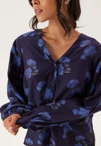 Marinblå långärmad blus med blommönster, med V-ringning och knappstängning. Tyget verkar mjukt med lätt struktur.