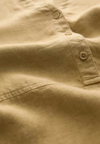 Senf-farbenes Leinenhemd mit strukturiertem Finish, ausgestattet mit zwei Knöpfen an der Knopfleiste und einem umgeschlagenen Rand für ein sauberes Design.