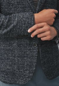 Blazer din amestec de lână, de culoare bleumarin, cu un model texturat, în dungi. Prezintă un singur nasture și o croială ajustată, având o buzunar pe partea stângă a pieptului.