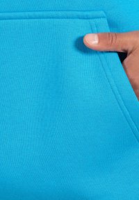 Sudadera de color turquesa con una textura suave, con un bolsillo en la parte delantera y una mano descansando en el borde del bolsillo.
