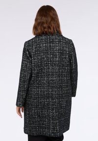 Cappotto in tweed bianco e nero con un design strutturato, maniche lunghe e vestibilità dritta; presenta un delicato motivo testurizzato.