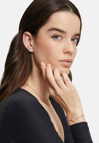 Orecchini d'argento con tre perle bianche, un bracciale abbinato con perle e una delicata catena d'argento, indossati da una modella con capelli lunghi fino alle spalle.