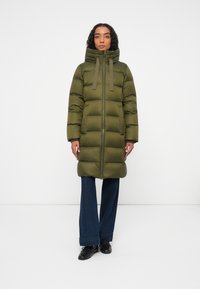 Chaqueta de plumas de color verde oliva, con un alto cuello, cremallera frontal y grandes bafles horizontales. Equipado con cordones y puños acanalados.