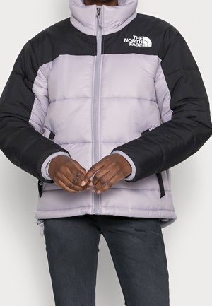 Veste matelassée en lavande clair avec des épaules noires, fermeture éclair sur le devant et poches latérales. Comprend un col montant et un design matelassé.