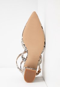 Sandale à talons aiguilles avec un bout pointu, dotée d'un design en serpentin noir et blanc, de brides beiges et d'une semelle striée pour une traction optimale.