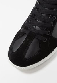 Černé tenisky s kombinací semišových a kožených materiálů, kulatou špičkou, texturovanými akcenty a bílou gumovou podrážkou.