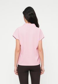 Πολο μπλουζάκι με κοντά μανίκια σε απαλό ροζ ύφασμα, με κλασικό γιακά, άνετη εφαρμογή και ελάχιστες ραφές. Συνδυάζεται με σκούρο κολάν.