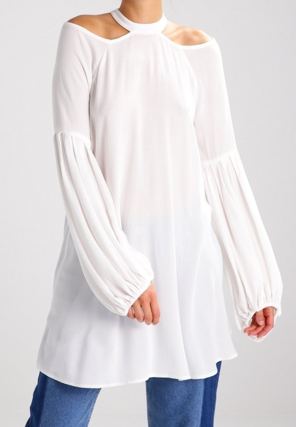 Vit långärmad topp med design för kalla axlar, samlade puffärmar och hög hals. Tillverkad av ett lätt, flödande tyg.